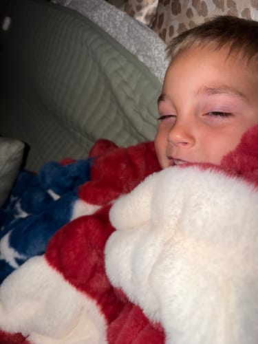 Close-up of a customer's child smiling while wrapped in the plush Hugs Flag Blanket.