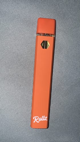 A customer's orange ROLLZ THCA Vape pen lying on a grey textured surface.