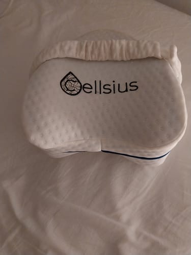Le coussin genoux Cellsius d'un client, avec sa housse blanche texturée, posé sur un lit.