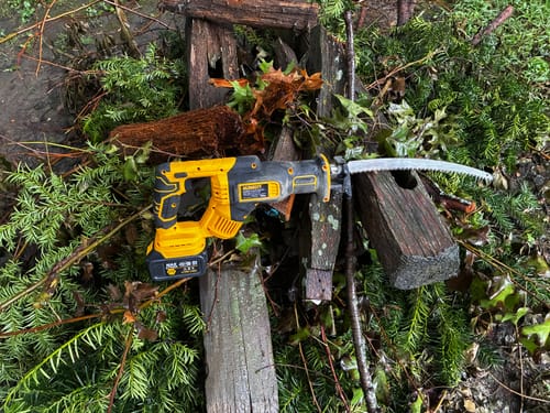 Customer's yellow reciprocating saw with a Japanese teeth arc blade, resting on scattered wood and branches outdoors.