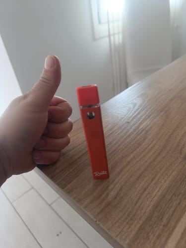 Reviewer's hand giving a thumbs up next to the orange ROLLZ THCA Vape on a wooden table.