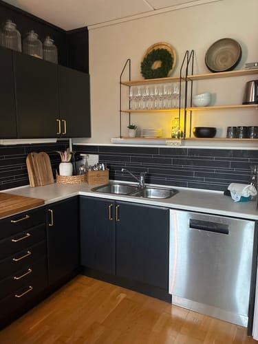 Reviewer's Treverk sort matt kontaktplast on kitchen cabinets with gold handles and a view of the sink area.