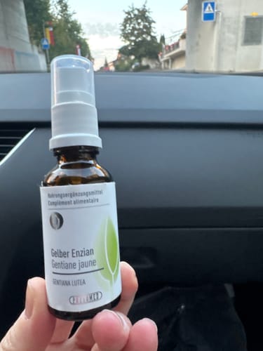 Kundenfoto des Phytomed Knospenextrakt Gelber Enzian Sprays, gehalten in einer Hand vor einem Autocockpit.
