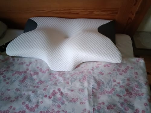 Customer's white and gray ergonomic memory foam pillow placed on a bed.