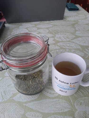 Customer's Thymiankraut Tee in einem Vorratsglas neben einer Tasse fertigem Thymiantee auf einem gemusterten Tisch.