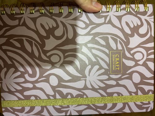 Customer's Cuaderno Mediano Líneas notebook featuring a patterned cover, spiral binding, and gold elastic band.