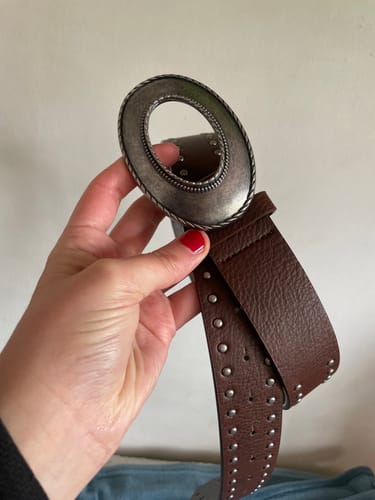 Customer's brown Cinturón Tachas Hebilla Maxi con tachuelas metálicas y hebilla ovalada en una mano.