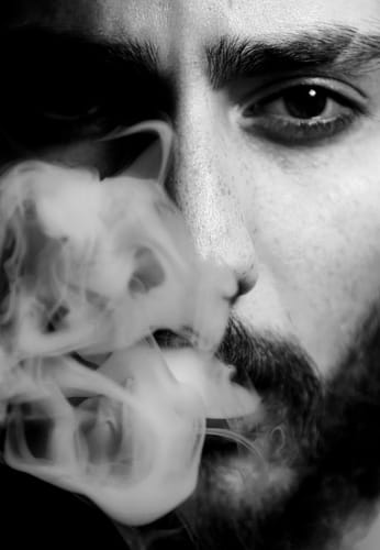 Reviewer exhaling vapor from a THC-A vape, face partially in shadow