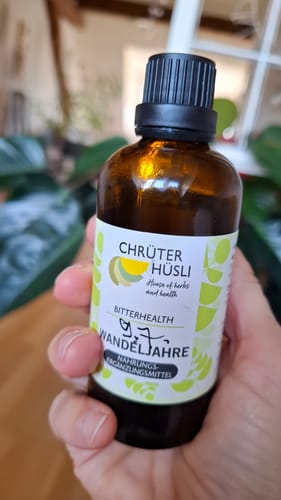 Customer's Hand holding the Wandeljahre 100 ml dark glass bottle with a white label in an indoor setting.