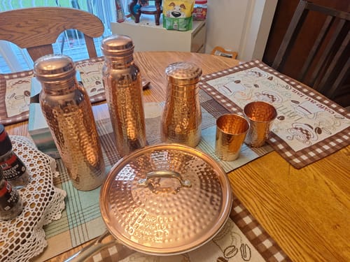 Customer's hammered copper bottles, cups, and cooking pot on a dining table.