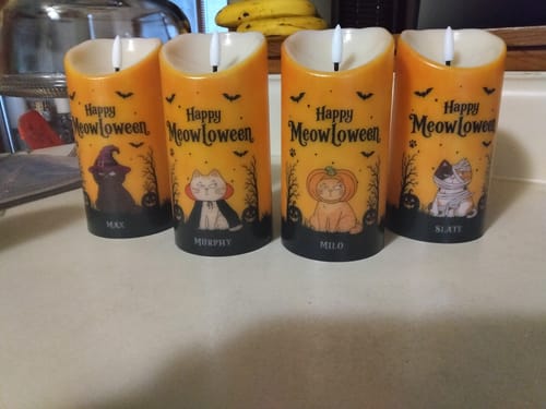 Customer's four personalized orange LED candles with cat illustrations and names on a white counter.