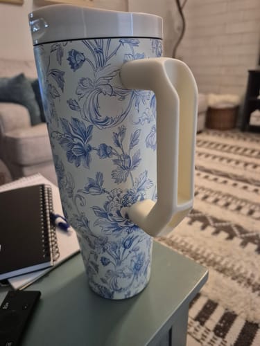 Reviewer's Thicc Buddy mug in blue floral pattern, featuring a sturdy cream handle and white lid on a desk.