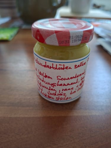 Customer's selbstgemachte Holunderblütensalbe aus gereinigtem Bienenwachs in einem kleinen Glas mit rot-weißem Deckel.