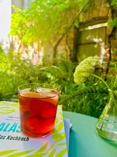 Kundenfoto des Pink Flamingo Eistees als rötliches Getränk in einem Glas auf einem Tisch im Garten