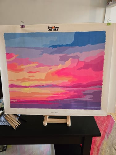Customer's Neon Pink Sunset paint-by-numbers canvas showing a colorful sunset scene on an easel.