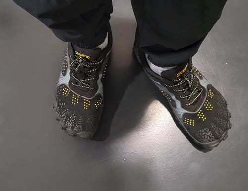Customer's black Fast I Pro Barfußschuhe on feet, showing the flexible design and yellow accents.