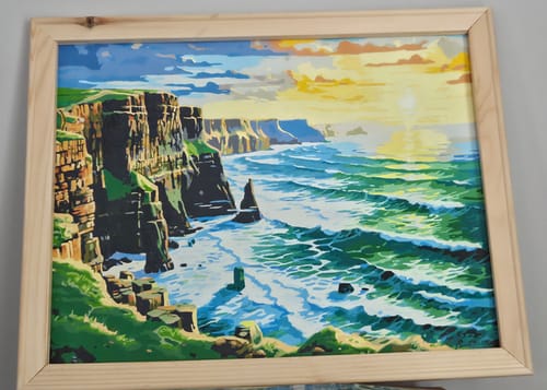 Reviewer's finished Cliffside Sunset Waves paint by numbers kit framed, showcasing vibrant coastal sunset scenery.