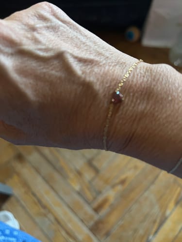 Customer's delicate gold bracelet with a small heart charm worn on their wrist.