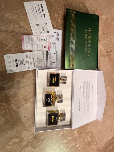 Customer's OUD Supreme BUNDLE box containing three glass perfume bottles and product cards on a stone surface.