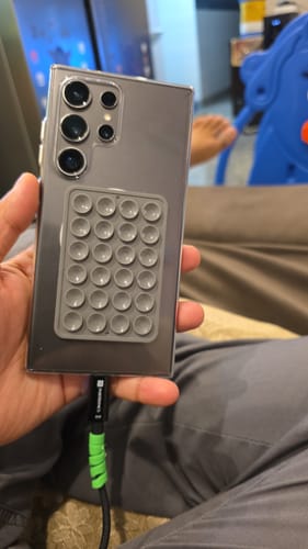 Customer's hand holding a phone case with a grey, multi-suction cup StickyPod mount attached to the back.