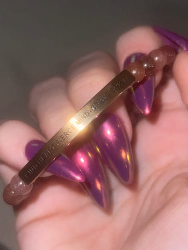 Reviewer's hand holding a rose-gold beaded bracelet with the engraved message KIND HEART - FIERCE MIND - BRAVE SPIRIT.