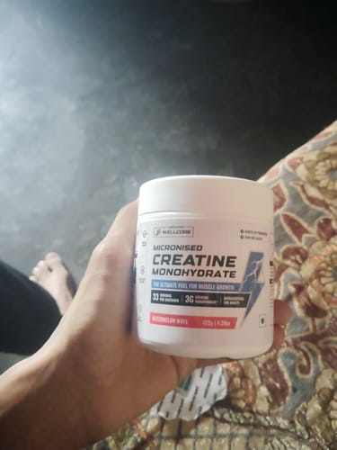 Customer's hand holding a white tub of Wellcore Micronised Creatine Monohydrate in Watermelon Wave flavor.