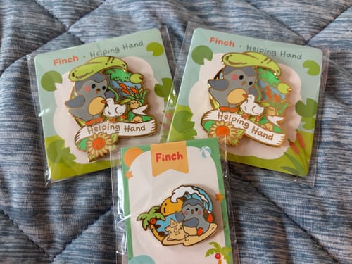Customer's Little Escape Pin shown in packaging alongside Helping Hand pins