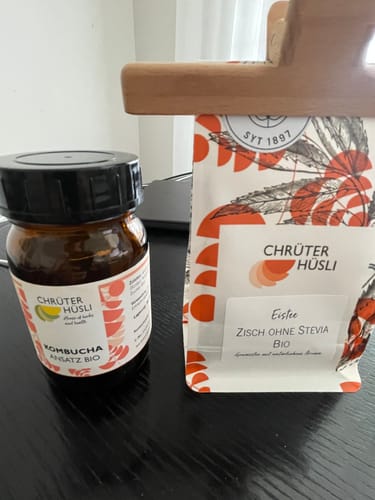 Customer's Eistee Zisch Bio Kräutertee Packung neben einer Flasche Kombucha Ansatz Bio auf einem Tisch.