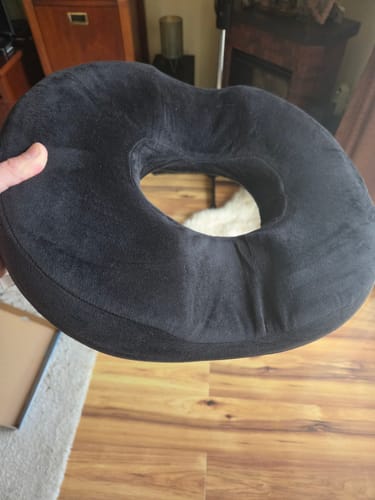 Customer's black, ergonomic prosztata pillow held by a hand in a room.