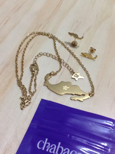 Customer's Set Mexico Lindo gold necklace and matching stud earrings resting on a wooden surface next to packaging.