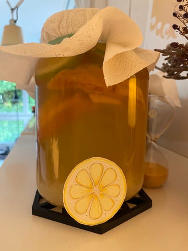Customer's Wasser Kefir Bioproduct fermenting in a large glass jar with a white paper cover, next to an hourglass.