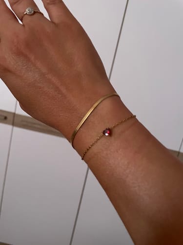 Customer's gold Love Bracelet worn on a wrist alongside a thin chain bracelet with a small heart charm.