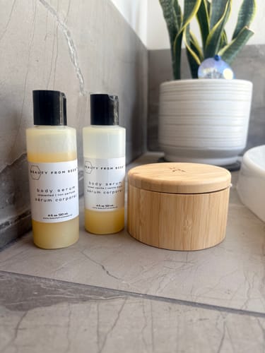 Customer's two Body Serum bottles and one wooden container on a bathroom counter with a plant.