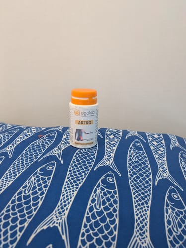 Customer's Artro supplement bottle placed on a blue surface with white fish patterns.
