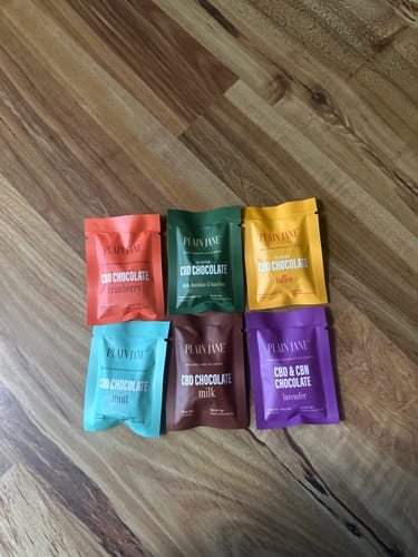 Reviewer's collection of six colorful Plain Jane CBD Chocolate Minis laid out on a wooden surface.