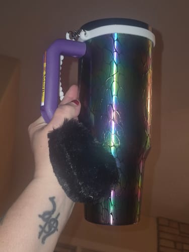 Customer's iridescent Thicc Buddy mug held by hand, featuring a purple handle and a black fuzzy charm.