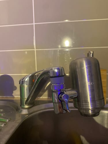 Customer's metallic BlissfulHome Tap Filter installed on a kitchen faucet against a tiled backsplash.