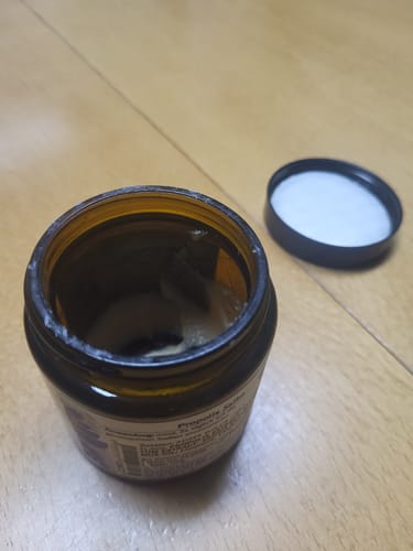 Customer's opened brown Propolis Salbe jar with the lid off on a wooden surface.