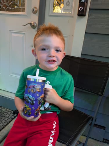 Customer's child holding a purple Peace & Love CREWCUP featuring a monster truck print.
