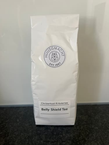 Customer's Belly Shield Tee product packaging showing the white herbal tea bag on a dark surface.