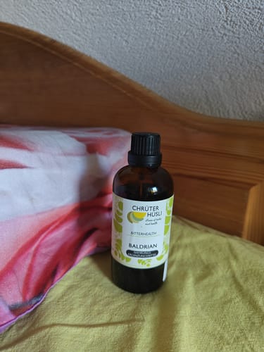Customer's Baldrian Tropfen amber glass bottle standing on a bed with bedding.