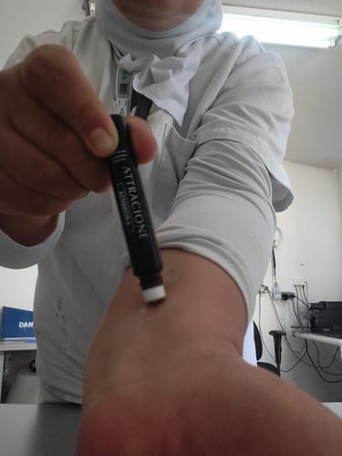 Customer's Ativador de Feromônios Attracione em um tubo preto sendo aplicado na pele do braço.