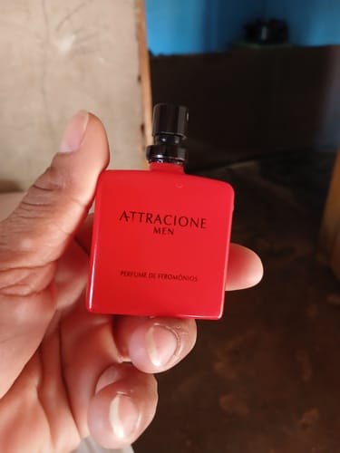 Customer's hand holding a red rectangular Attracione Men perfume bottle with black cap.