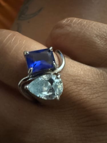Customer's Navae Birthstone Ring on a finger, featuring a pear-cut light blue stone and a rectangle-cut dark blue stone.