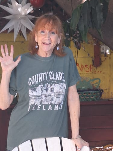 Reviewer smiling and waving while wearing the spruce green County Clare T-Shirt in a casual outdoor setting.