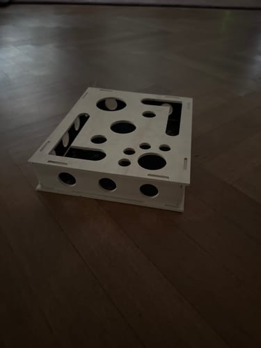 Reviewer's Schleif-Jagdbox wooden cat toy with various cut-out shapes, placed on a wooden floor.