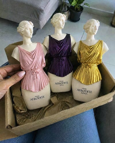 Customer's Kit Afrodite perfume bottles in pink, purple, and gold, held in a hand inside an open box.