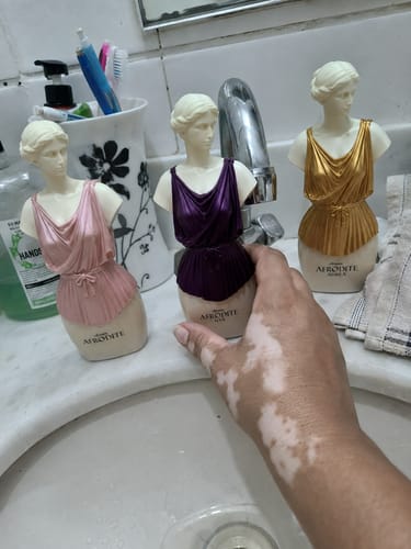 Reviewer's three Kit Afrodite perfume bottles in bust shapes, in rose, dark purple, and gold, standing on a bathroom sink.