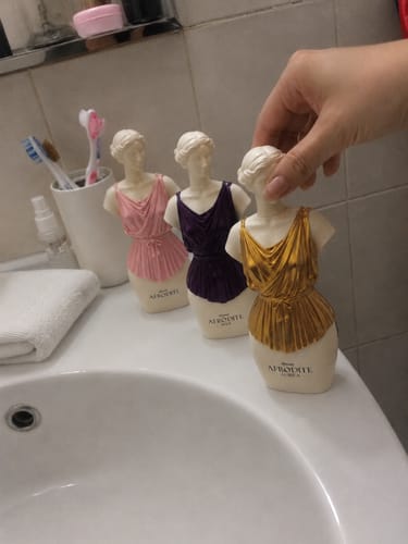 Customer's Kit Afrodite perfume bottles in pink, purple, and gold bust shapes held by a hand on a bathroom counter.