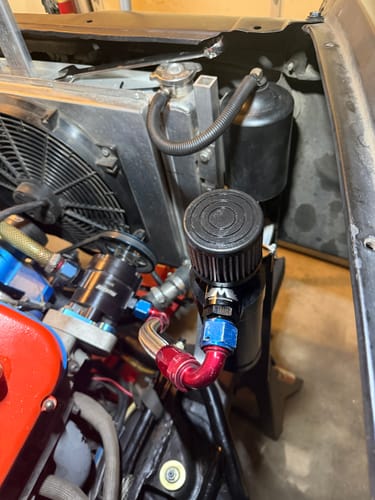 Customer's black Billet XL catch can installed in an engine bay with red and blue fittings.